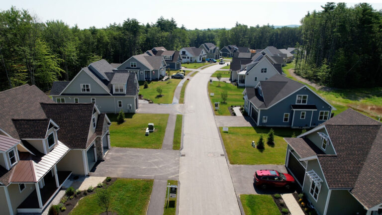 Aerial view down Lady Walsingham Way showing completed homes at Lady of the Lakes Estates surrounded by wooded conservation land in Laconia, New Hampshire.