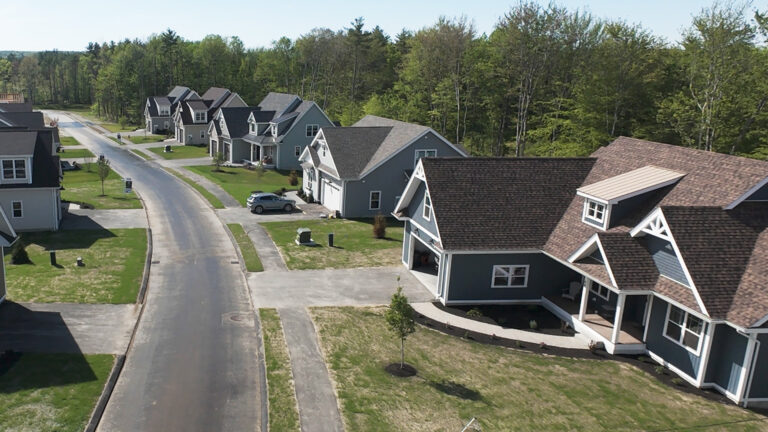 Aerial view along Lady Walsingham Way showing completed homes at Lady of the Lakes Estates surrounded by wooded conservation land in Laconia, New Hampshire.